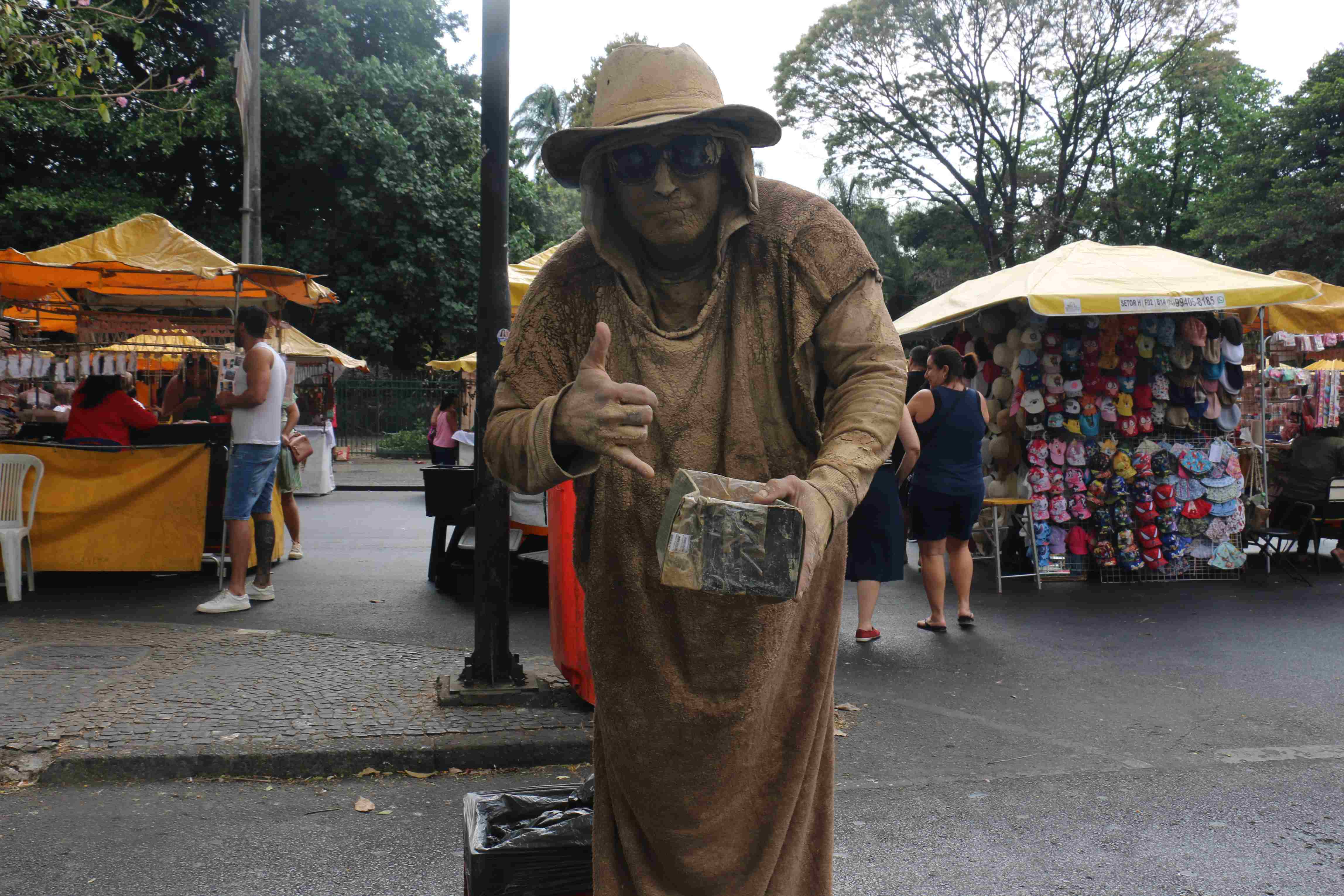 Artista que faz a performance de uma estatua viva coberta de "lama" posando para a foto.