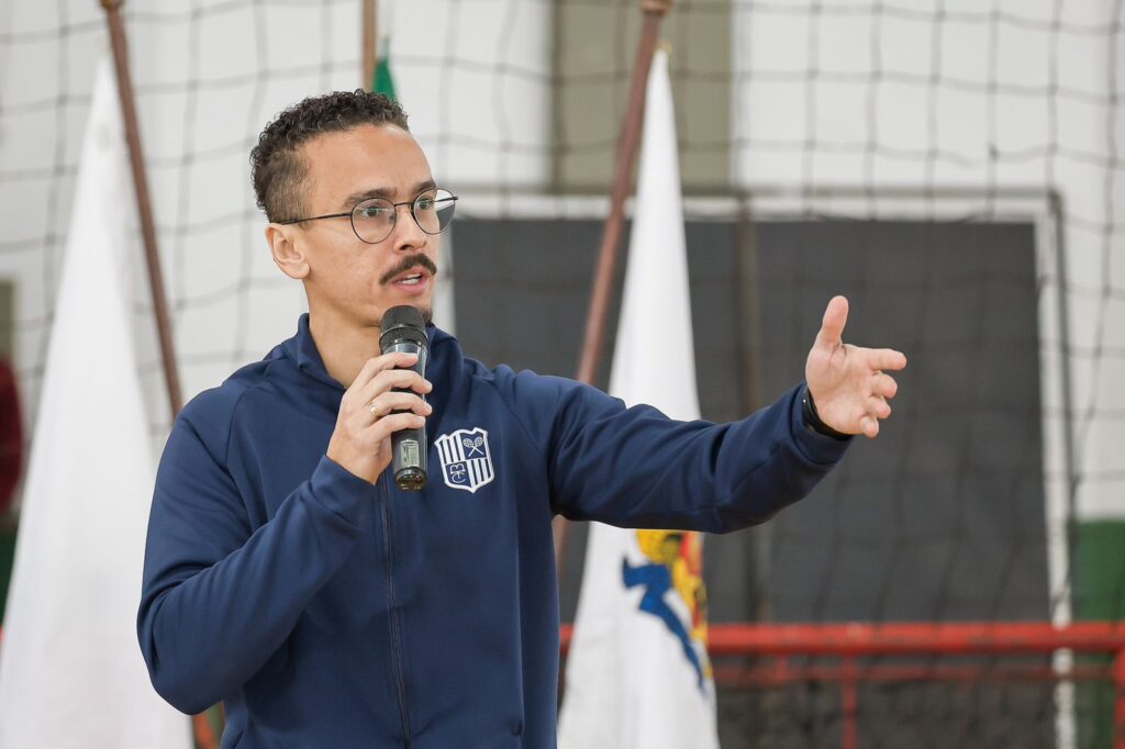 Coordenador das Escolas de Esportes do Minas Tênis Clube com um microfone na mão e gesticulando enquanto fazia um discurso