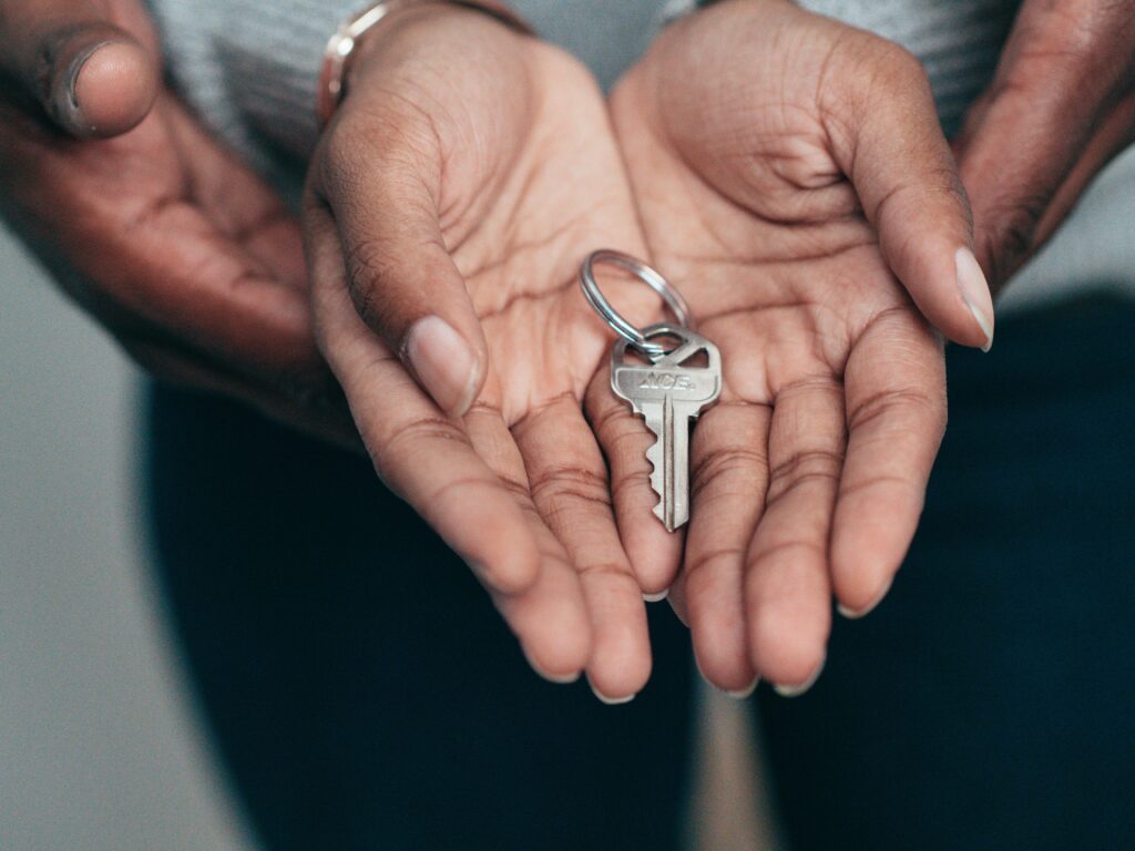 Duas mãos abertas, uma sob a outra, com uma chave de casa dentro