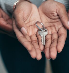 Duas mãos abertas, uma sob a outra, com uma chave de casa dentro