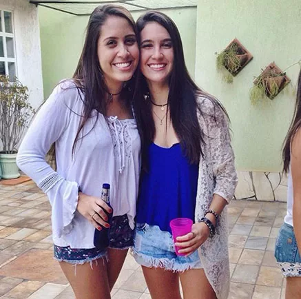 Mariana e sua amiga Isabela posam sorrindo lado a lado. As duas estão com roupas casuais e descontraídas. O clima da imagem é de intimidade e amizade, com fundo neutro e iluminação suave.
