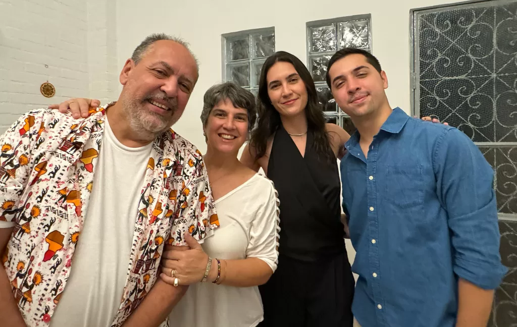 Foto de família com 4 pessoas brancas, em pé, sorrindo. Dois homens e duas mulheres, entre elas Mariana Spinelli