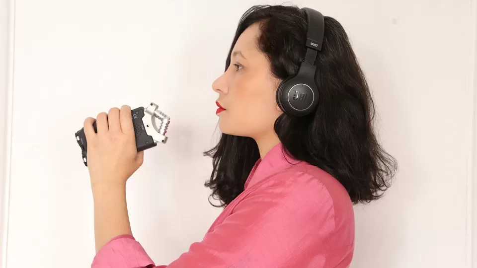 Carol Pires em perfil, segurando um microfone e usando fone de ouvido.