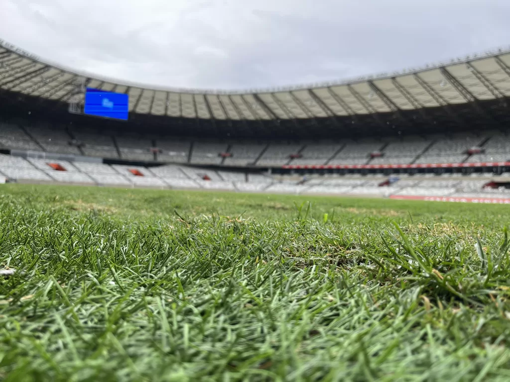 Gramado verde ocupa metade inferior da foto e ao fundo o estádio mineirão e o céu