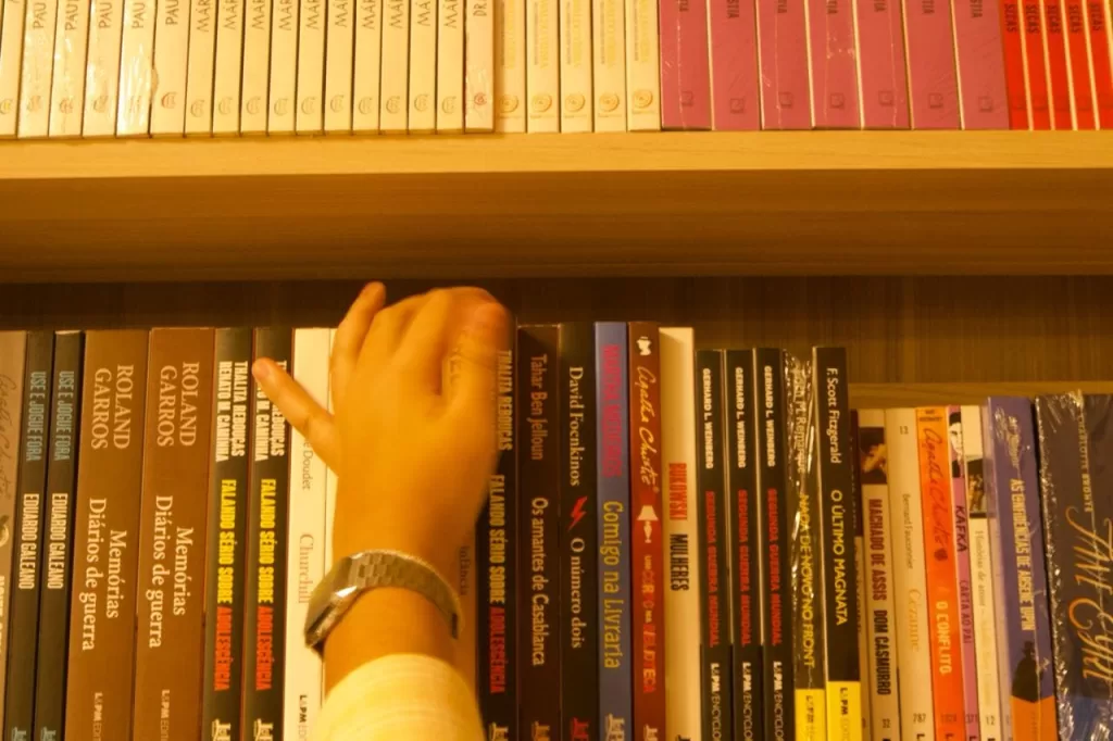 Pessoa pegando livro na estante de uma livraria