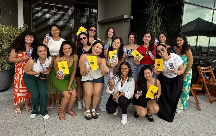 Foto com dezesseis mulheres juntas segurando um livro amarelo