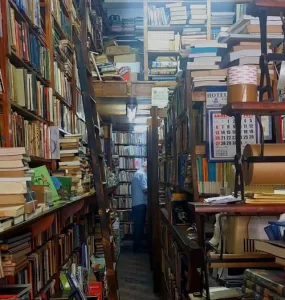 A foto mostra os fundos de uma livraria com prateleiras cheias de livro do chão ao teto.