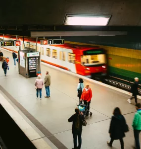 Metrô vermelho em movimento rápido passando por uma estação moderna com plataforma iluminada e poucos passageiros.