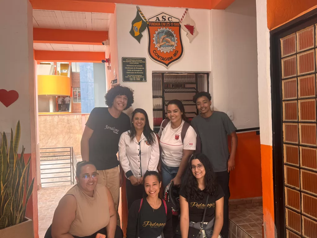 Larissa Miranda ao centro, rodeada por estudantes de Pedagogia e Jornalismo. Ao fundo, o brasão da ASC. Créditos: Vinicios Braga