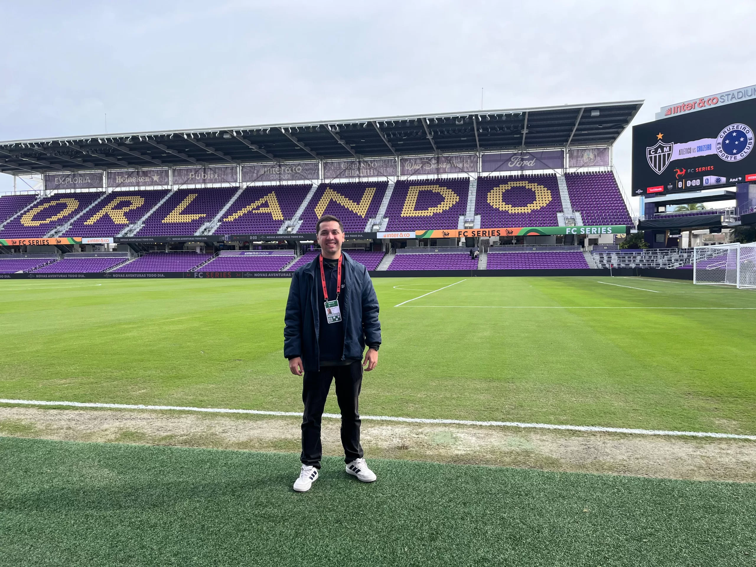 Um homem no centro da foto em um estádio de futebol. Ao fundo, a arquibancada em roxo escrito "ORLANDO".