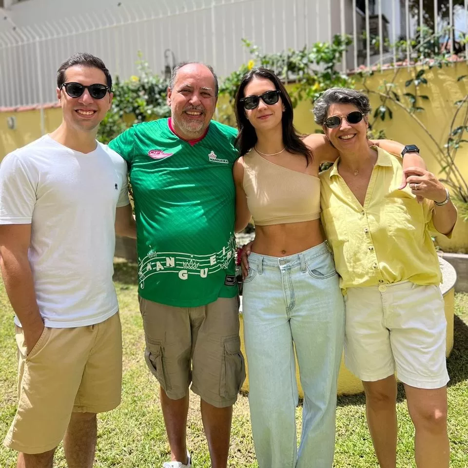 Foto de família com 4 pessoas brancas, em pé no sol, sorrindo. Dois homens e duas mulheres