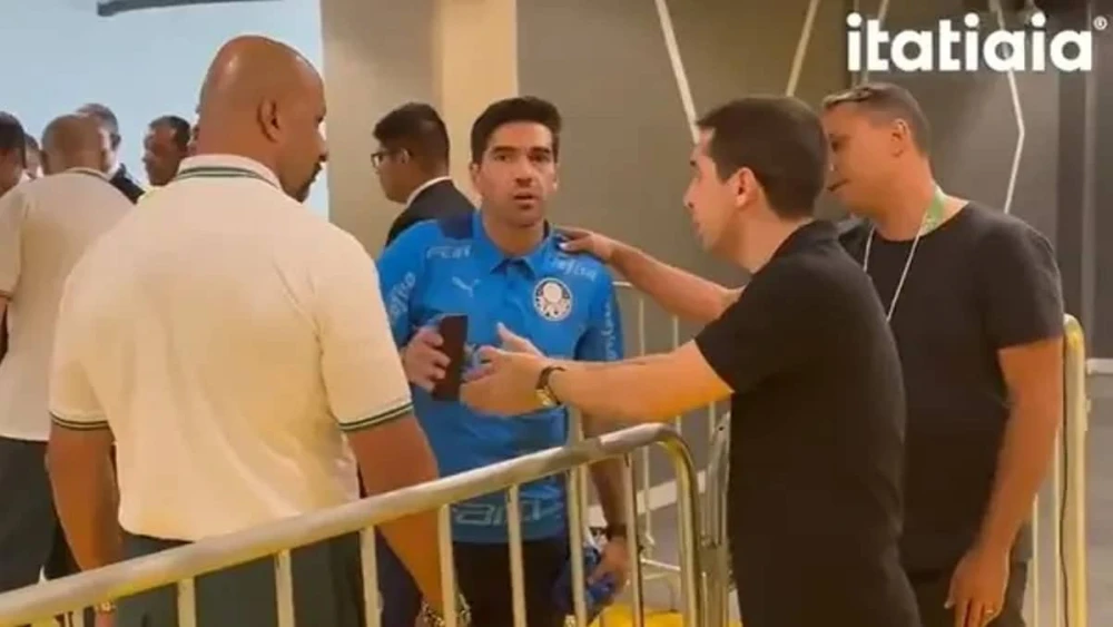 Na foto tem quatro homens. Um deles está segurando o celular enquanto o que está em sua frente tenta pegar o aparelho. Os outros dois observam a cena.