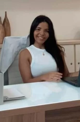 Ana é uma mulher jovem, sentada na mesa do seu escritório com o rosto sorridente