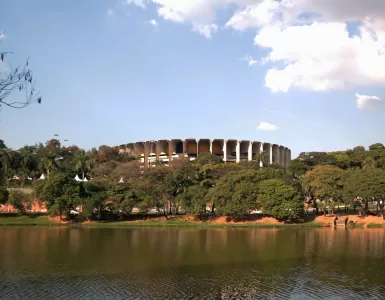 Imagem panorâmica da Lagoa da Pampulha em Belo Horizonte, com o Ginásio Mineirinho ao fundo, vegetação nas margens e céu azul, representando a revitalização da região e o projeto de retomada da navegação.