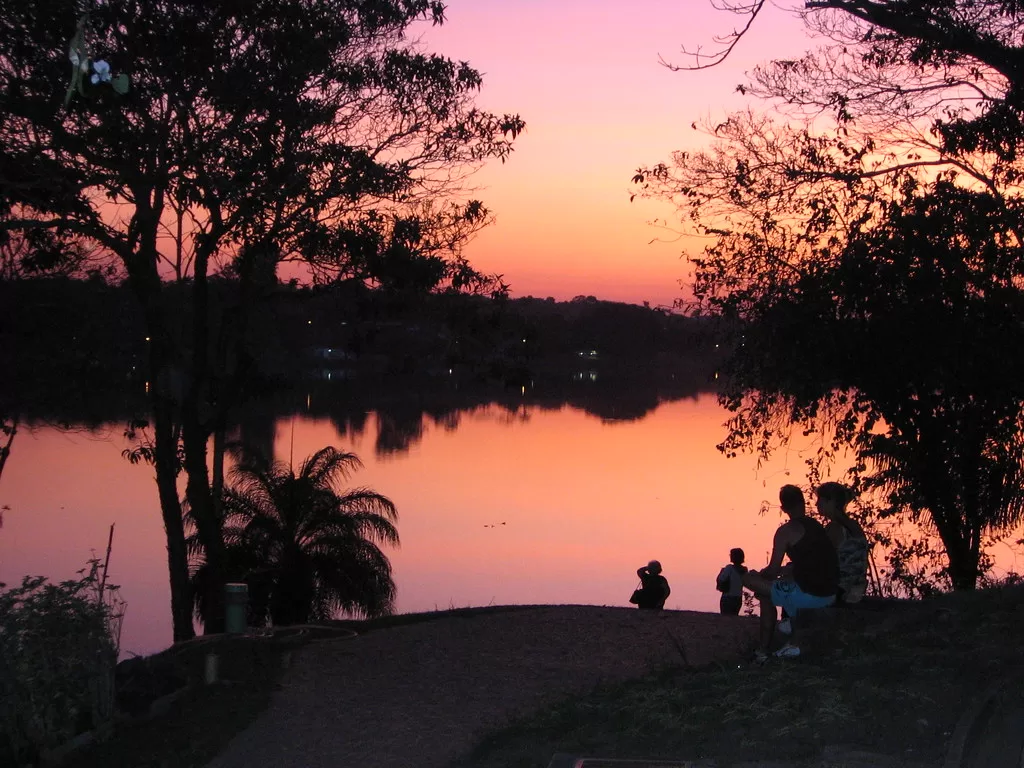 Pôr do sol na Lagoa da Pampulha, em Belo Horizonte, com o Estádio Mineirão ao fundo e o reflexo do céu alaranjado nas águas.