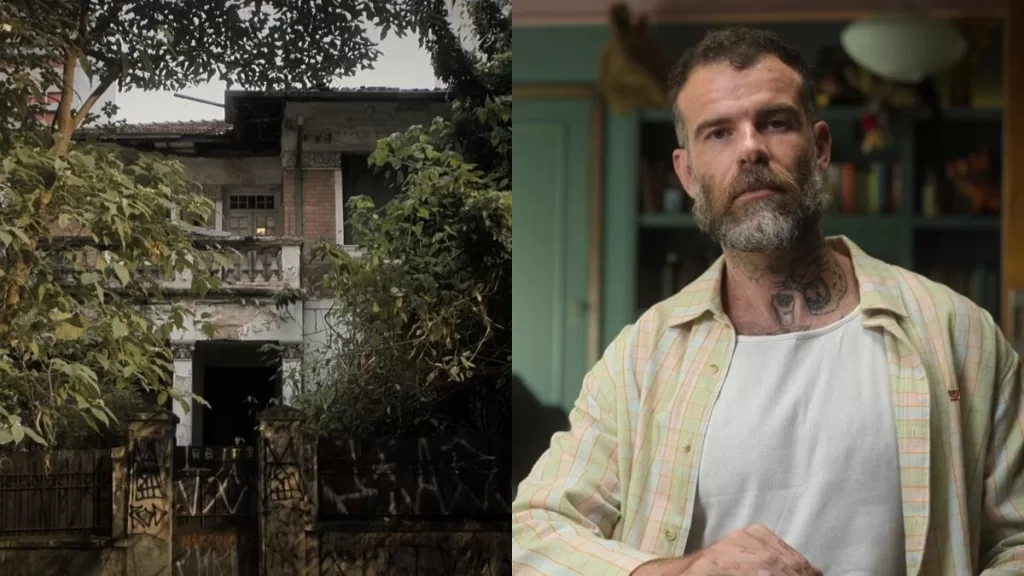 A imagem é dividida em duas partes. A parte da esquerda mostra uma casa antiga coberta por vegetação de ambos os lados, com sua fachada grafitada e uma estrutura desgastada. Na parte da direita, observa-se Chico Felitti em primeiro plano, ele é branco, tem cabelo curto loiro escuro, usa uma regata simples de cor branca e uma camisa xadrez por cima dela. O cenário aparenta ser uma casa, com uma estante à direita de Chico, e uma parede verde escura ao fundo.