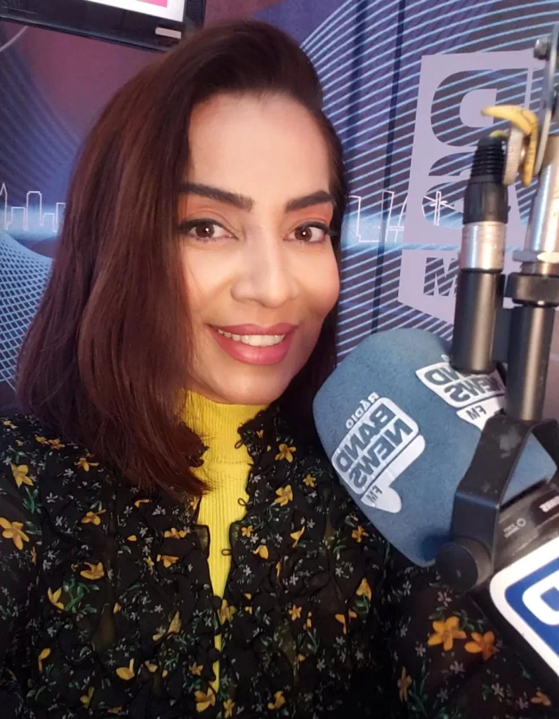 Foto colorida, com sorriso de Vianna em primeiro plano frente a um
microfone de estúdio. Em segundo plano está o estúdio de gravação da rádio Band
News iluminado por luzes brancas e azuis.