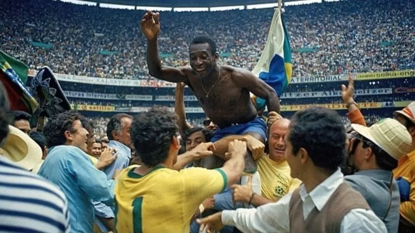 Pelé no centro da imagem sendo erguido e ovacionado pelo povo que entrou no campo após a conquista da Copa do Mundo de 1970. Ao fundo, as arquibancadas com vários torcedores.
