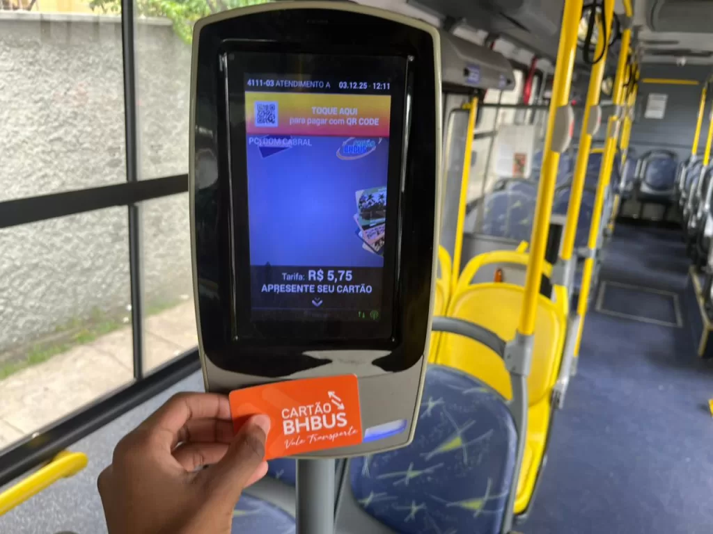 Dentro de um ônibus da linha 4111, um passageiro aproxima um cartão BHBus laranja de um validador eletrônico. A tela mostra a tarifa de R$ 5,75 e opções de pagamento. Ao fundo, aparecem os assentos.