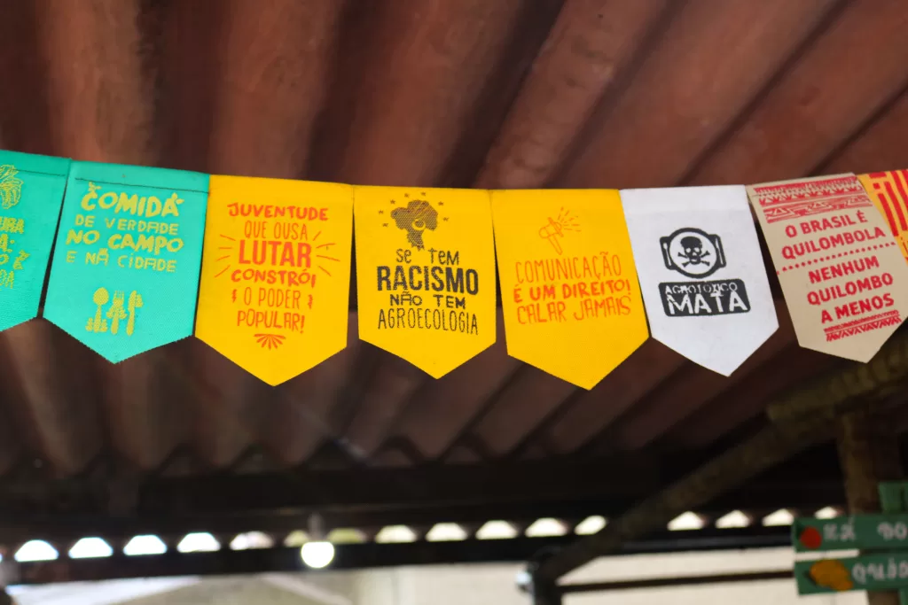 Bandeirinhas com mensagens político-sociais enfeitam a estrutura da feira, reforçando causas que caminham lado a lado à agroecologia e ao direito de comer bem.