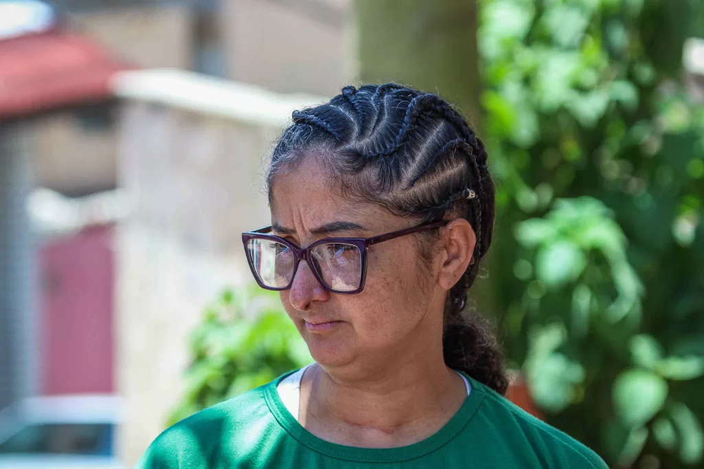 Raquel, uma mulher parda, de expressão solene. Ela usa óculos e tem o cabelo castanho em tranças. Veste uma blusa verde, do mercado onde trabalha.