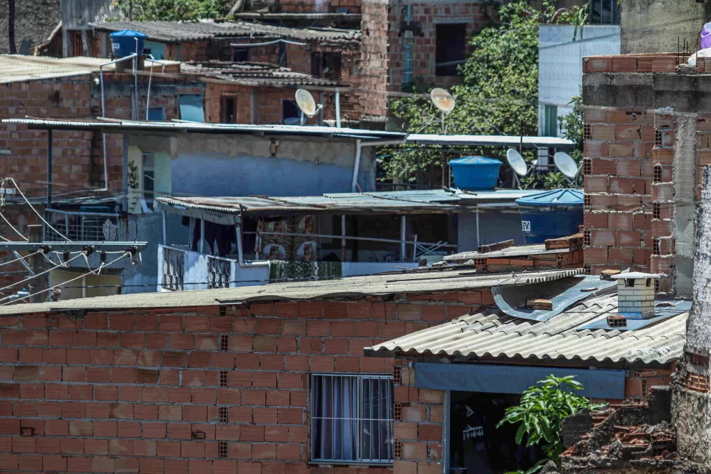 Vários telhados de casas no Morro do Papagaio. As casas são feitas de tijolos, e o telhado é fino. Apenas duas tem caixas d'água.