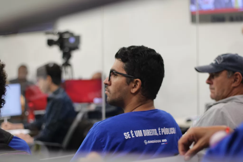 Homem de costas, acompanhando audiência na ALMG, com a frase "Se é um direito, é público" nas costas