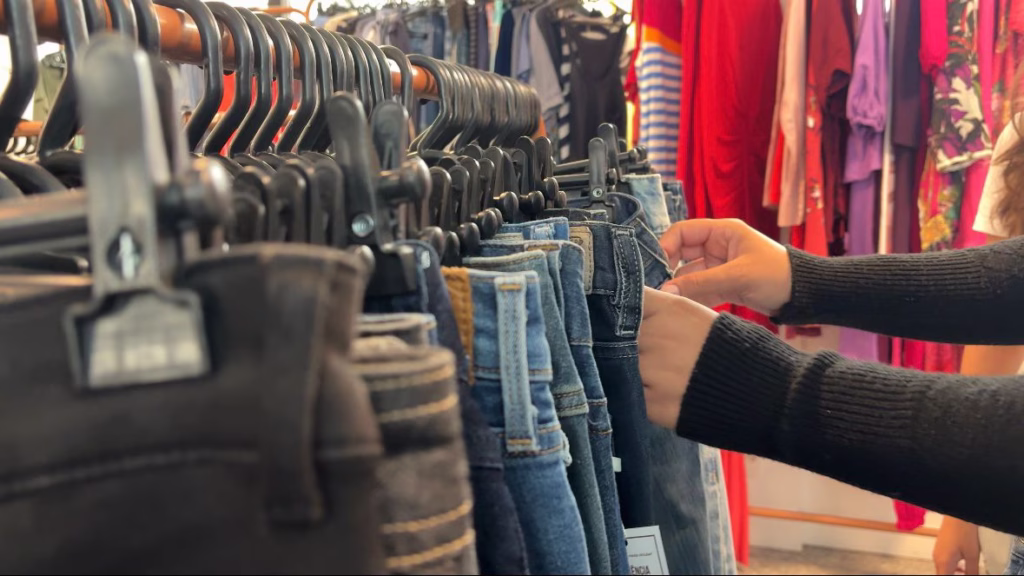 Pessoa seleciona roupas em arara de brechó em Belo Horizonte